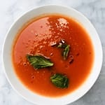 A bowl of tomato soup with basil and olive oil.