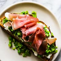 A thick piece of toast piled high with burrata, peas and prosciutto.