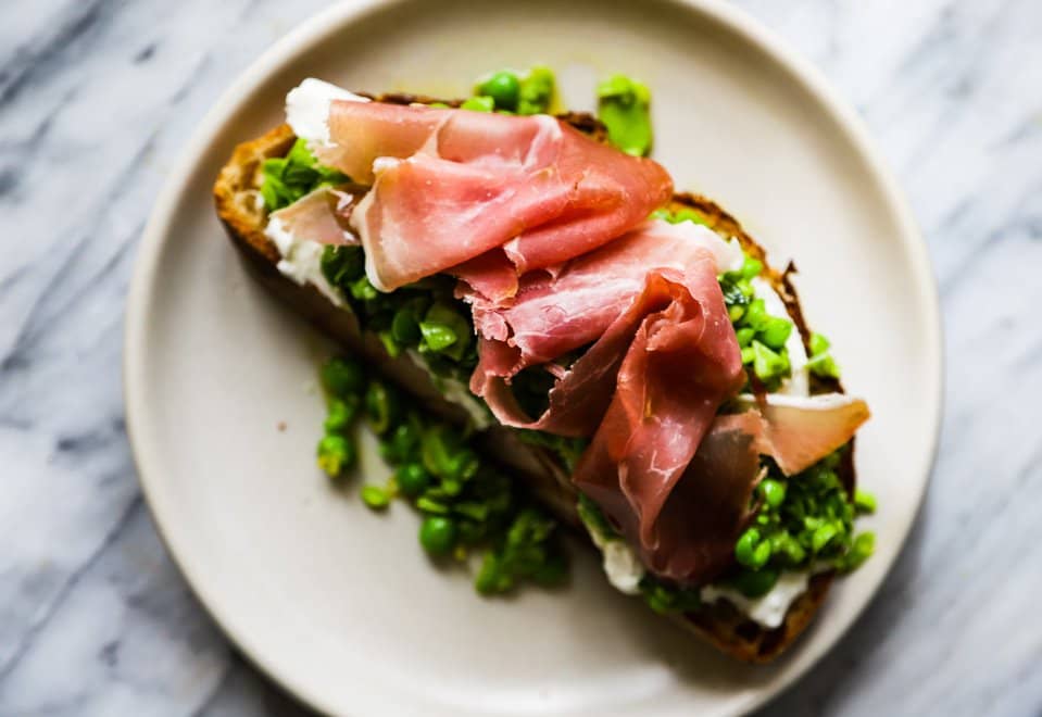 A thick piece of toast piled high with burrata, peas and prosciutto.